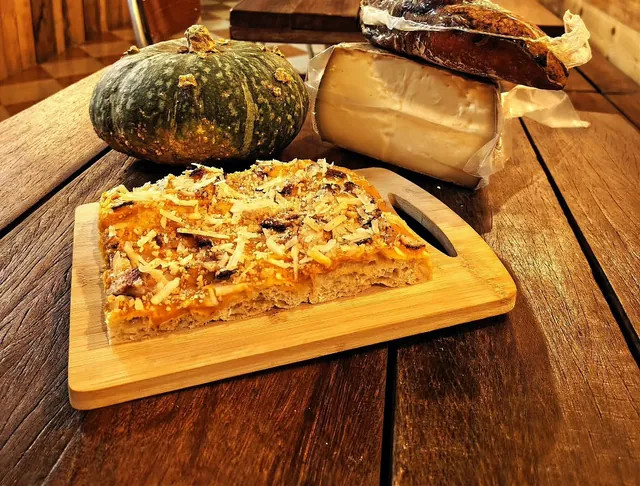 Un trancio di pizza al taglio con crema di zucca, pecorino, guanciale e noci, su un tagliere nel locale